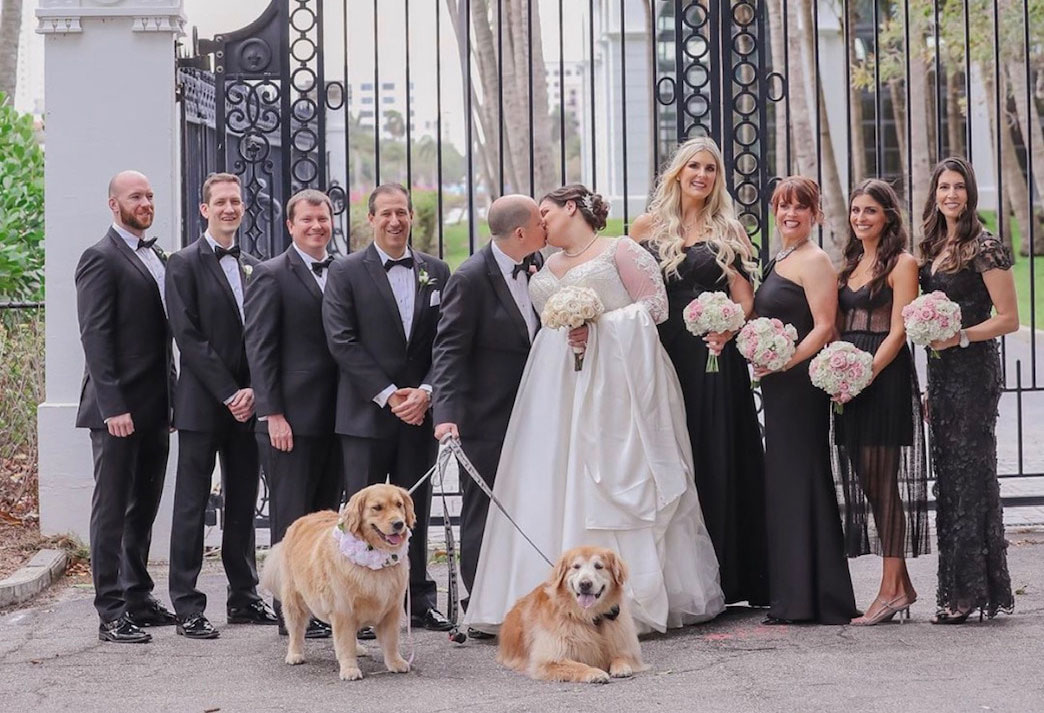 group at a wedding posing for camera using furever us wedding day dog care, two golden retrievers in from