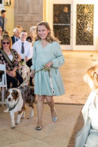 wedding dog sitter walking white, brown and grey dog down the aisle. Woman has a teal short dress on.